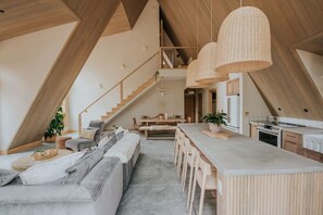 A modern interior with a dining area, kitchen, and a staircase leading to an upper level. - *NEW* Luxury A-Frame by Sunday River w/ hot tub (Bethel)