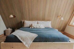 A bedroom with a sloped ceiling, a bed with a blue bedspread, two white pillows, and two wall-mounted lamps. - *NEW* Luxury A-Frame by Sunday River w/ hot tub (Bethel)