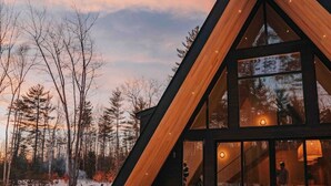 A modern cabin with a sloped roof, large windows, and a snow-covered landscape. - *NEW* Luxury A-Frame by Sunday River w/ hot tub (Bethel)