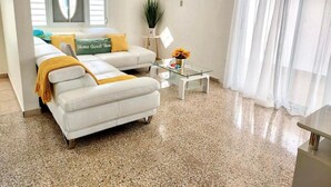 Una sala de estar con un sofá blanco, una mesa de centro de vidrio y una planta en maceta.