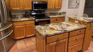 A kitchen with wooden cabinets, a stainless steel refrigerator, a microwave, and granite countertops.