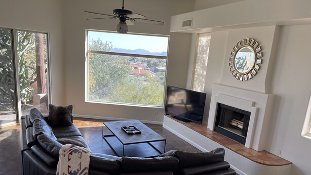 A modern living room with a sectional sofa, a flat-screen TV, a fireplace, and a large window offering a view of the outdoors.