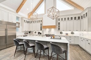 A modern kitchen with a large island, white cabinetry, and a wooden ceiling.