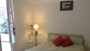 Quarto com cama, mesa de cabeceira com abajur, quadro na parede e janela com cortinas.