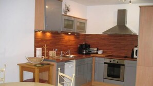 Uma cozinha compacta com painel de madeira, eletrodomésticos de aço inoxidável e um espaço de refeições com mesa redonda e cadeiras.