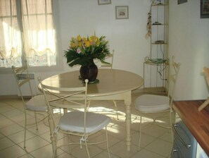 Un comedor con una mesa redonda, cuatro sillas, un florero con flores y una ventana con cortinas.