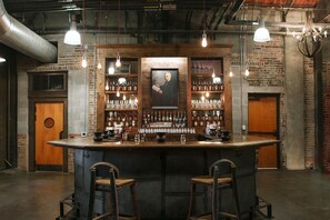 A bar area with a wooden counter, stools, and shelves stocked with bottles and glasses.