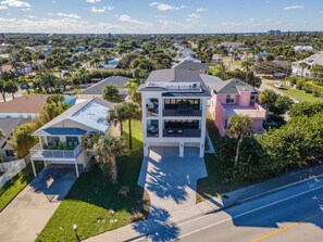 Un edificio residencial de varios pisos con balcón y piscina, rodeado de palmeras y otras viviendas.