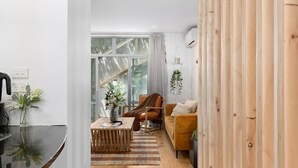 Ein modernes Wohnzimmer mit einer Couch, einem Couchtisch und einem Sessel. Es gibt ein Fenster mit Vorhängen, eine Pflanze und eine Pendelleuchte.