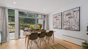 Ein Essbereich mit einem Holztisch, vier Stühlen und Blick auf einen Wald durch große Fenster.