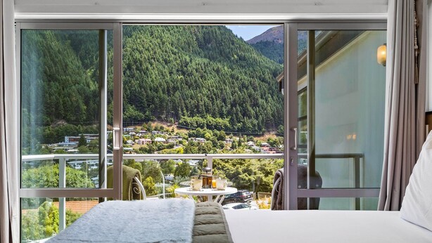 Ein Schlafzimmer mit großem Fenster, das einen Blick auf einen bewaldeten Berg und ein Dorf weiter unten freigibt.