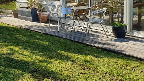Une maison moderne dotée d’un patio entièrement vitré, de meubles d’extérieur et de plantes en pot.