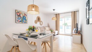 A modern dining area with a glass table, white chairs, and a hanging light fixture. - 2-Bedroom Apartment with Direct Beach Access & Private Parking – Estepona (Estepona)