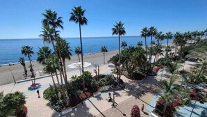A beachside resort with palm trees, a paved walkway, and a view of the ocean. - 2-Bedroom Apartment with Direct Beach Access & Private Parking – Estepona (Estepona)