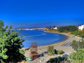 Une scène de plage côtière avec une tour de surveillance, des parasols et un ciel bleu dégagé.