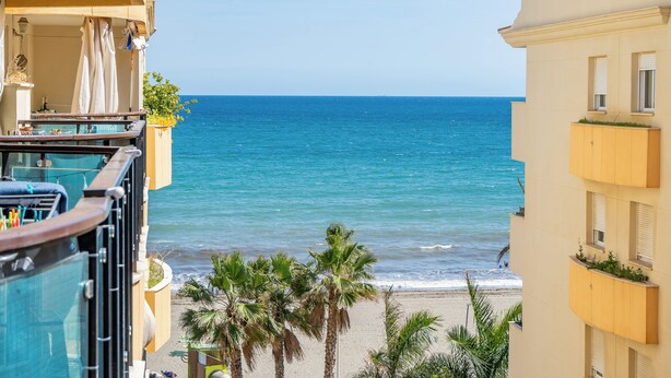 A balcony with a pool, overlooking a beach with palm trees and a clear blue sea. - 2-Bedroom Apartment with Direct Beach Access & Private Parking – Estepona (Estepona)