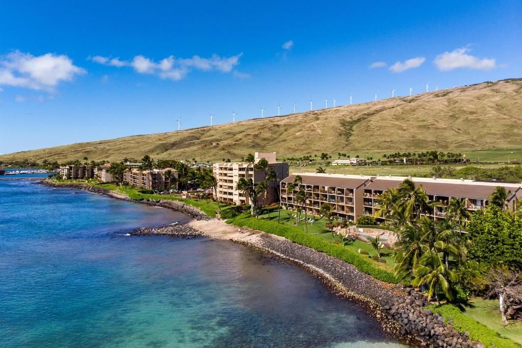 A coastal hotel with multiple buildings, a beach, and wind turbines in the background.
