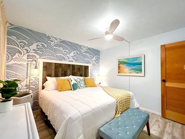 Un dormitorio con cama, mesita de noche, lámpara y una pared con diseño de olas.