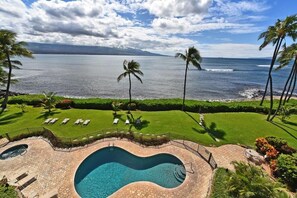 A swimming pool with a heart-shaped design, surrounded by a stone deck, with a view of the ocean and palm trees.