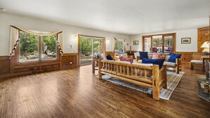 Una habitación amplia con suelo de madera, un banco grande de madera y varias ventanas con vistas al exterior.