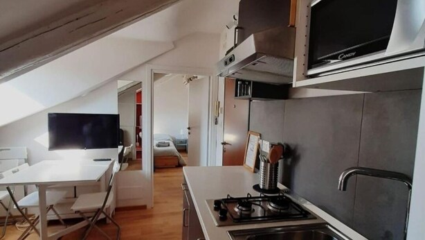 A modern kitchen with a gas stove, stainless steel sink, and a microwave. There is a dining area with a table and chairs, and a bedroom visible through an open door. - Casa Breton (Turin)