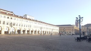 A spacious cobblestone plaza with historic buildings, a statue, and outdoor seating areas. - Casa Breton (Turin)