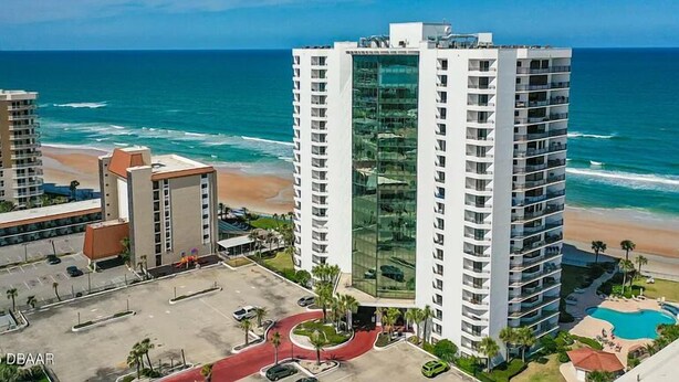 A high-rise hotel with a glass facade overlooking the beach. - Fantastic and completely updated direct ocean front condo at the Caribbean (Daytona Beach Shores)