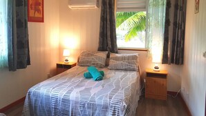 Un dormitorio con una cama, dos mesitas de noche, aire acondicionado, una ventana con cortinas y una lámpara de pared.