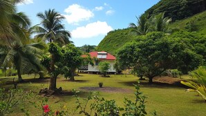 Un jardín exuberante con palmeras, un edificio de techo rojo y una colina al fondo.