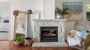 Una sala acogedora con chimenea de piedra, un sillón de mimbre y un cuadro de una playa.