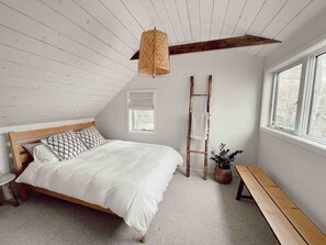 Un dormitorio con una cama de madera, un banco, una escalera y una lámpara colgante.