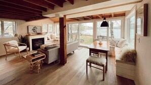 A spacious living room with a fireplace, wooden beams, large windows, and a cozy seating area. - Maine lake front ski getaway! (Greenwood)