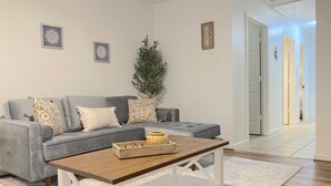 Uma sala de estar com um sofá cinza, uma mesa de centro de madeira e um vaso de planta.