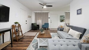 Uma sala de estar moderna com um sofá cinzento, uma mesa de centro de madeira, uma poltrona azul e uma poltrona preta.