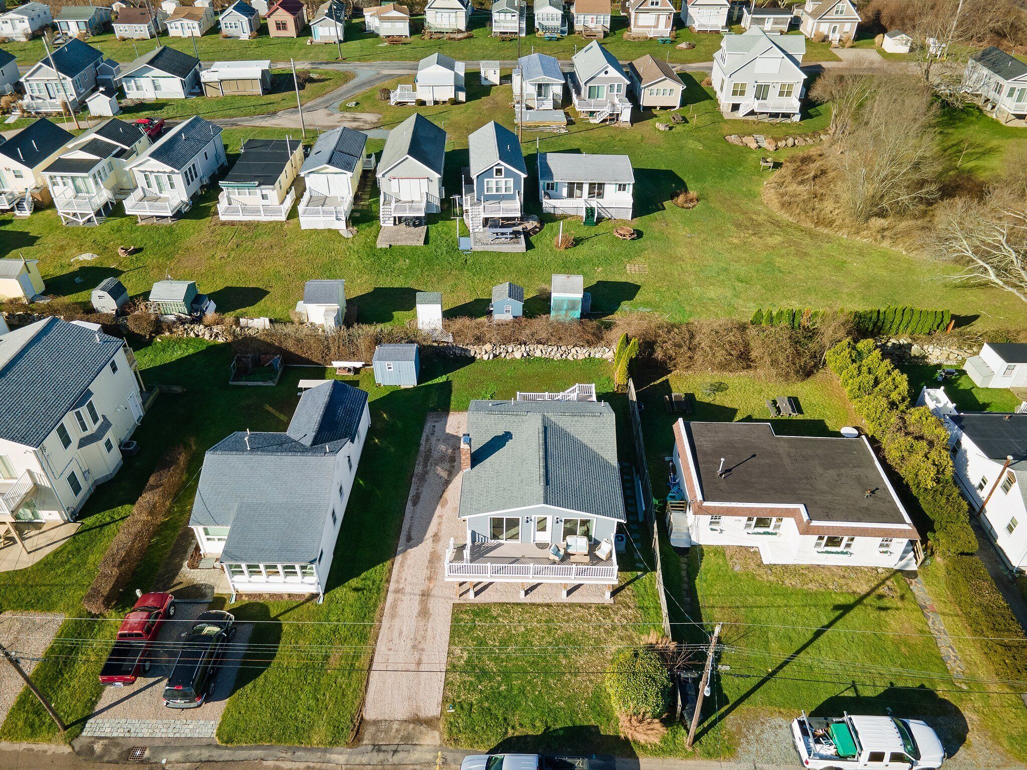 An aerial view of a residential area with multiple houses, a central road, and a few parked cars.