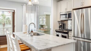A modern kitchen with a marble island, stainless steel appliances, and white cabinetry. - Hot Tub • Porches • Parking • Walk to King St! (Charleston)