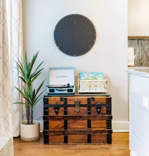 A wooden chest with a vintage design, a potted plant, a framed picture, and a wall-mounted decorative item. - Peaceful Porch • Parking • Walk to King St! (Charleston)