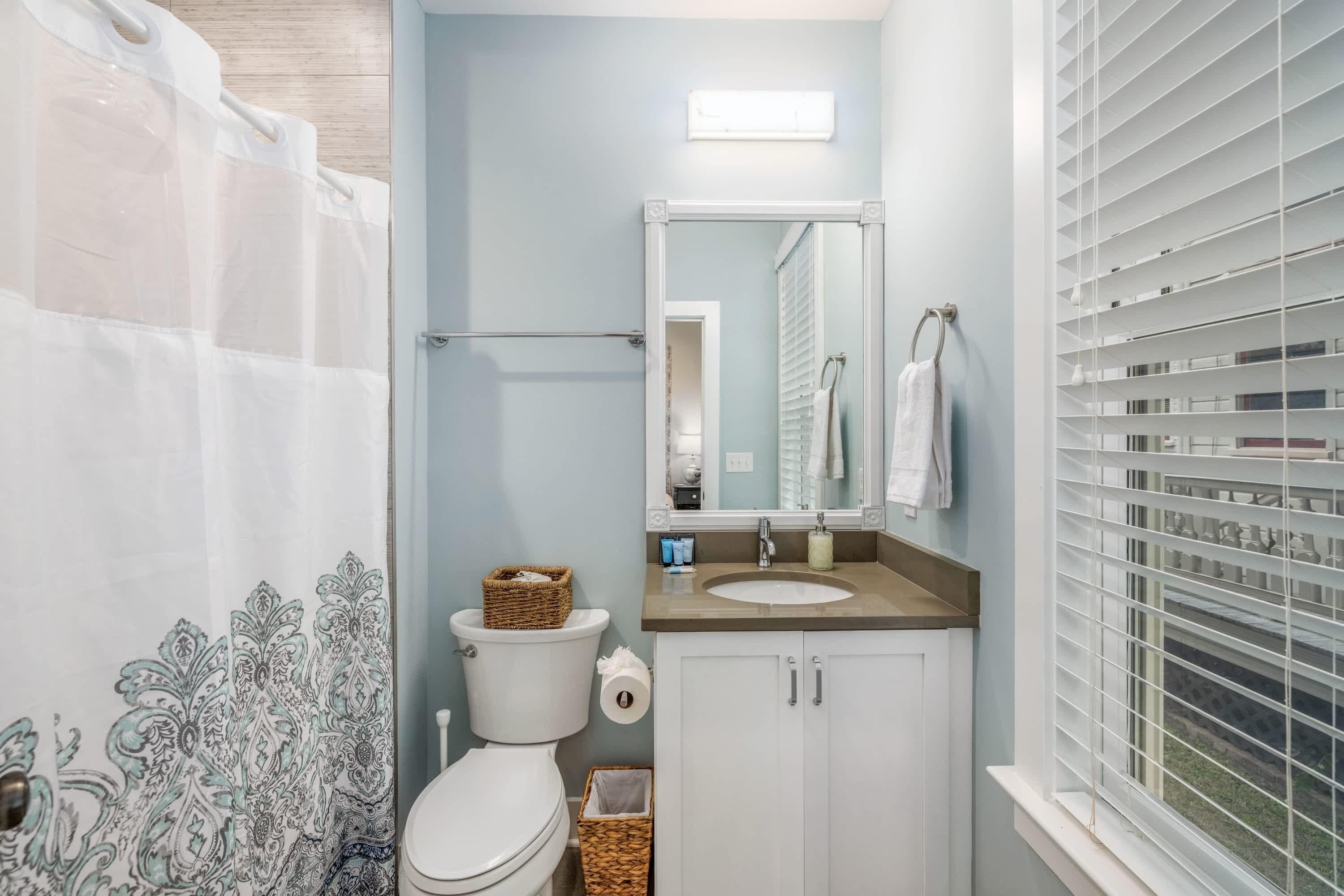 Une salle de bain avec des toilettes, un lavabo et une fenêtre équipée de stores.