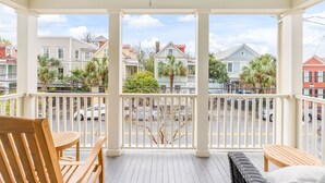 A covered porch with wooden furniture, a ceiling fan, and a view of neighboring houses and street.