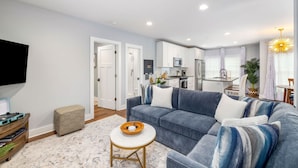 A modern living room with a grey sofa, a small round table, and a TV mounted on the wall. - Hot Tub Escape • Parking • Walk to King St! (Charleston)