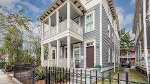A two-story residential building with a covered front porch, a visible door number, and a small front yard with a fence and plants. - Hot Tub Escape • Parking • Walk to King St! (Charleston)