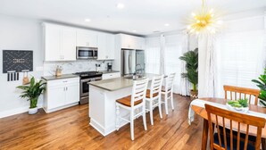 A modern kitchen with white cabinetry, stainless steel appliances, and a central island with bar stools. - Hot Tub Escape • Parking • Walk to King St! (Charleston)