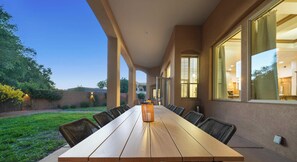 A covered outdoor dining area with a long table and chairs, large windows, and a view of the surrounding landscape.