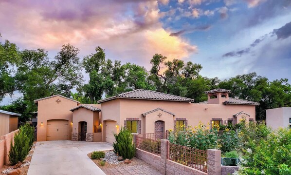 A stucco building with a tiled roof, a covered driveway, and a fenced garden area with sunflowers.