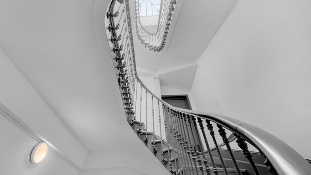 Una escalera de caracol con cerramiento de vidrio, barandilla de metal y una lámpara.