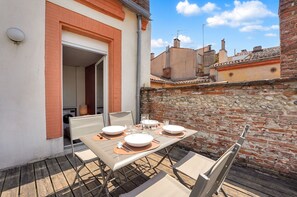 Un patio al aire libre con una mesa dispuesta para cuatro personas, rodeado de muros de ladrillo y un cielo despejado.