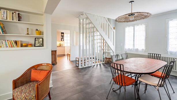 A dining area with a round table and chairs, a staircase, and a bookshelf with books and decorative items. - Ty Bigorn'oh - Three Bedroom House, Sleeps 7 (Benodet)