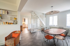 Uma sala de jantar com mesa redonda e cadeiras, escada e estante com livros e objetos decorativos.