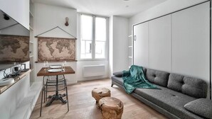 A modern living room with a grey sofa, a wooden dining table with chairs, a world map on the wall, and a hanging light fixture. - Magnifique studio - Le Marais (Paris)