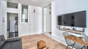A modern living room with a flat-screen TV, a dining table with chairs, a sofa, and a large window. - Magnifique studio - Le Marais (Paris)